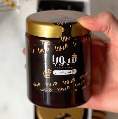 Hand holding a jar of coffee with a gold lid, featuring Arabic text.