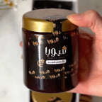 Hand holding a jar of coffee with a gold lid, featuring Arabic text.